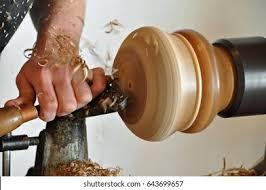 A picture of a hand holding a chisel and carving wood on a lathe.